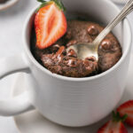 protein chocolate mug cake topped with chocolate chips and a strawberry slice with a spoonful being taken out