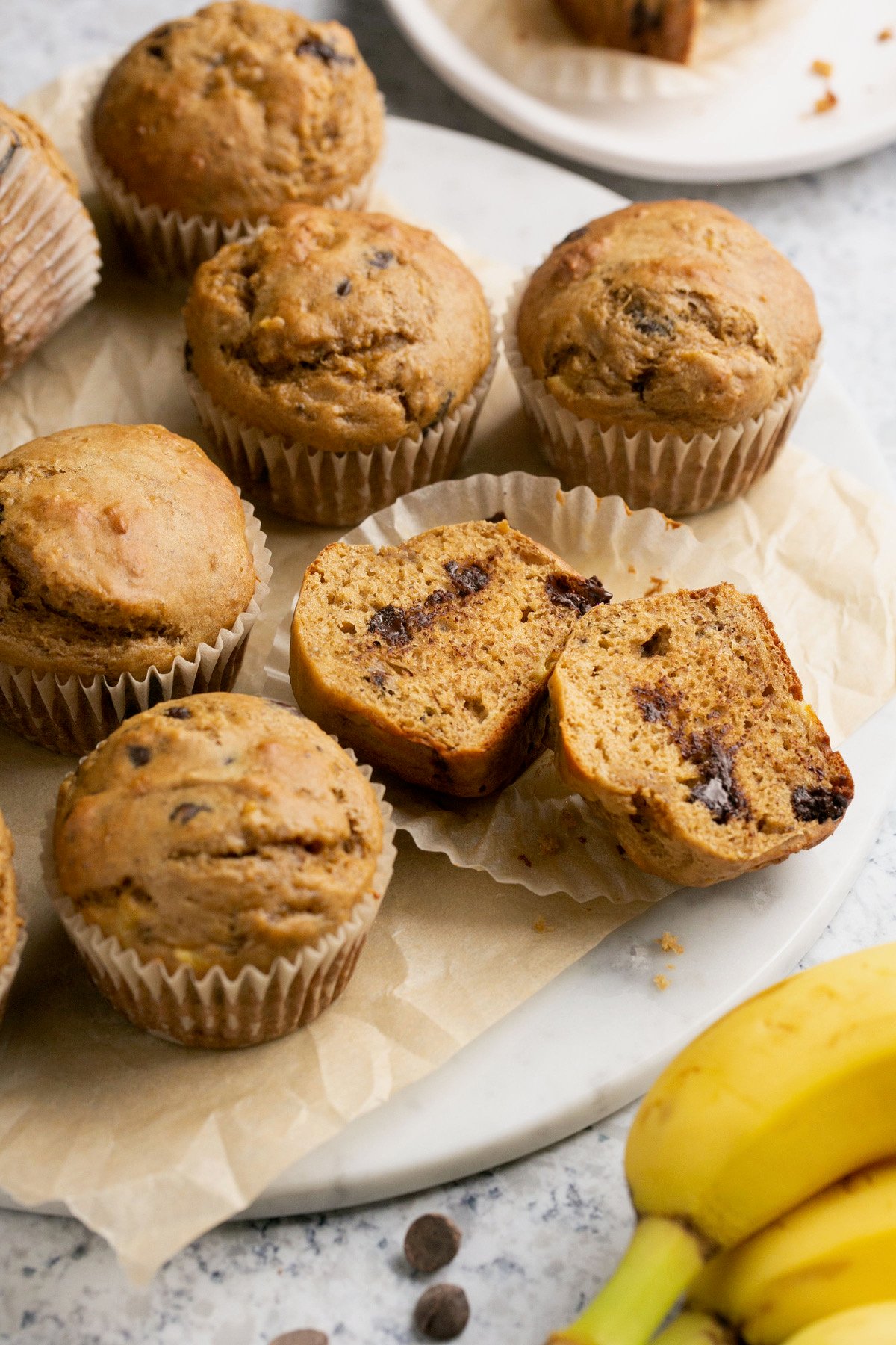 a close up shot of banana muffins wrapped in muffin lines with one sliced down the middle showing the inside