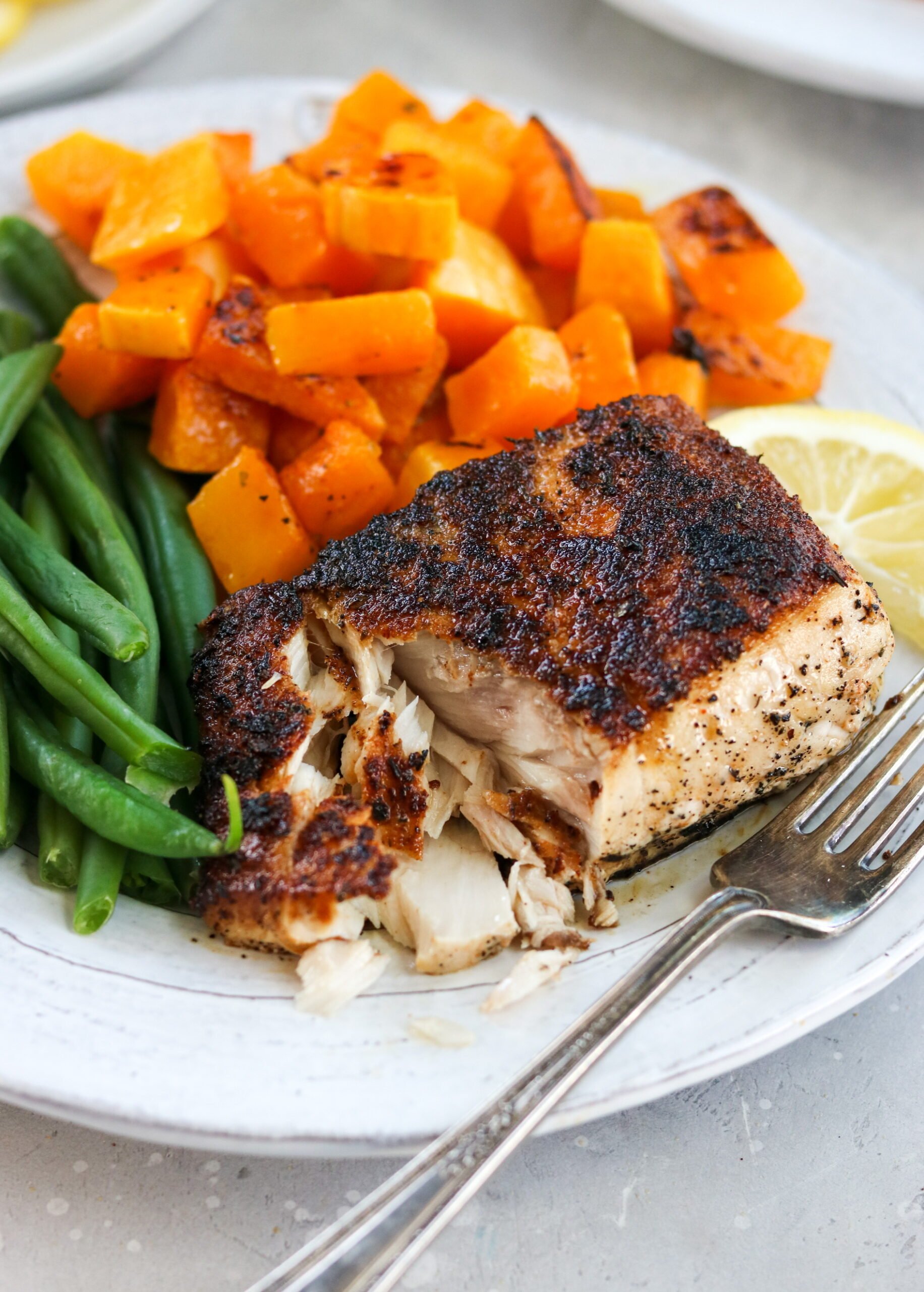 blackened mahi mahi on a plate with butternut squash and green beans with a fork flaking the fish apart