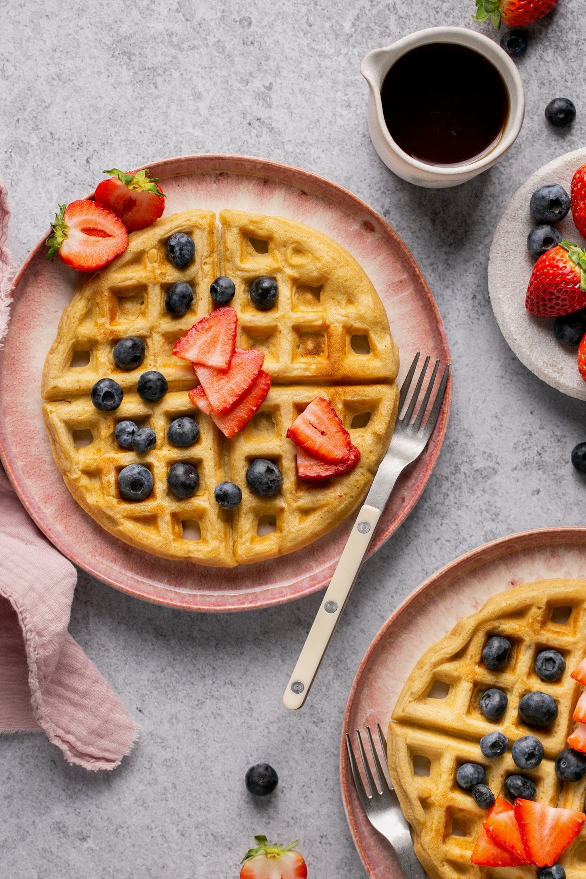 a gluten free waffle on a pink plate topped with blueberries and sliced strawberries