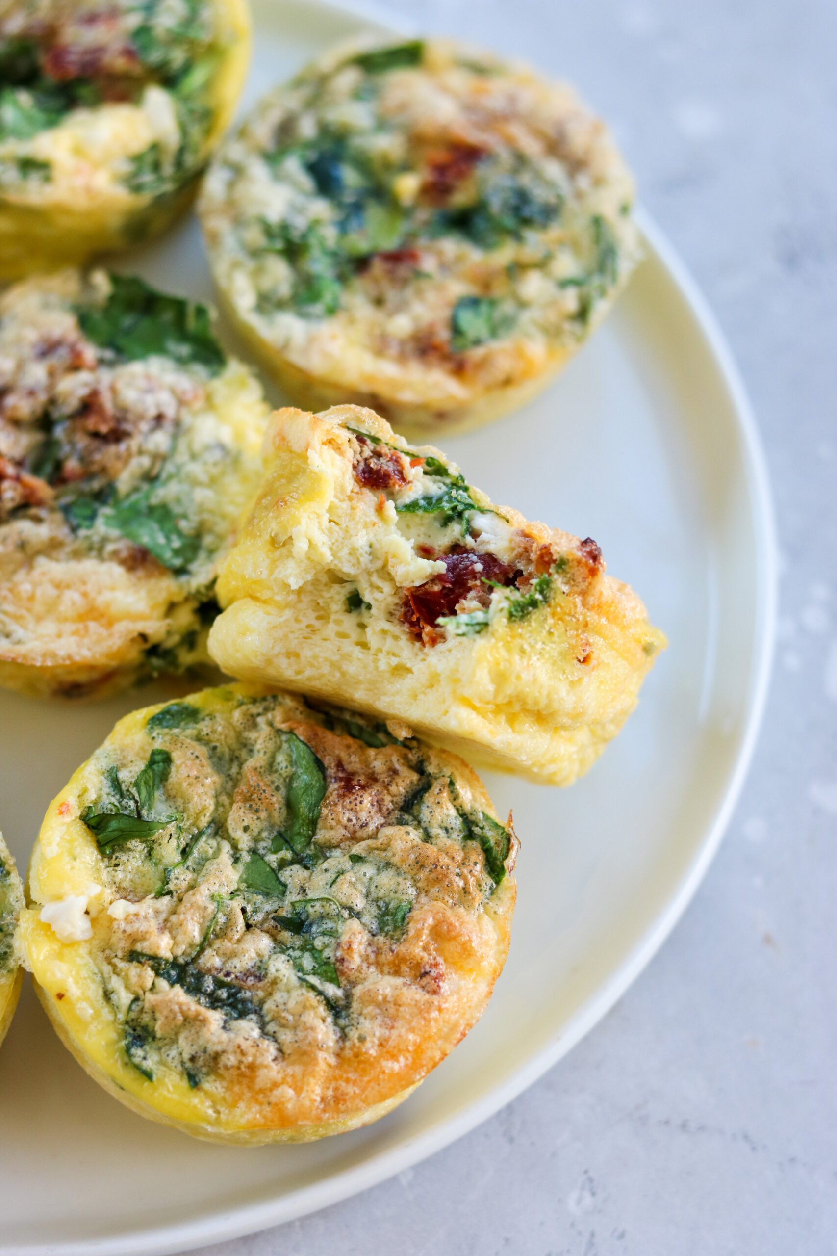 egg bites with spinach, feta, and sun dried tomatoes on a plate with a bite taken out of one