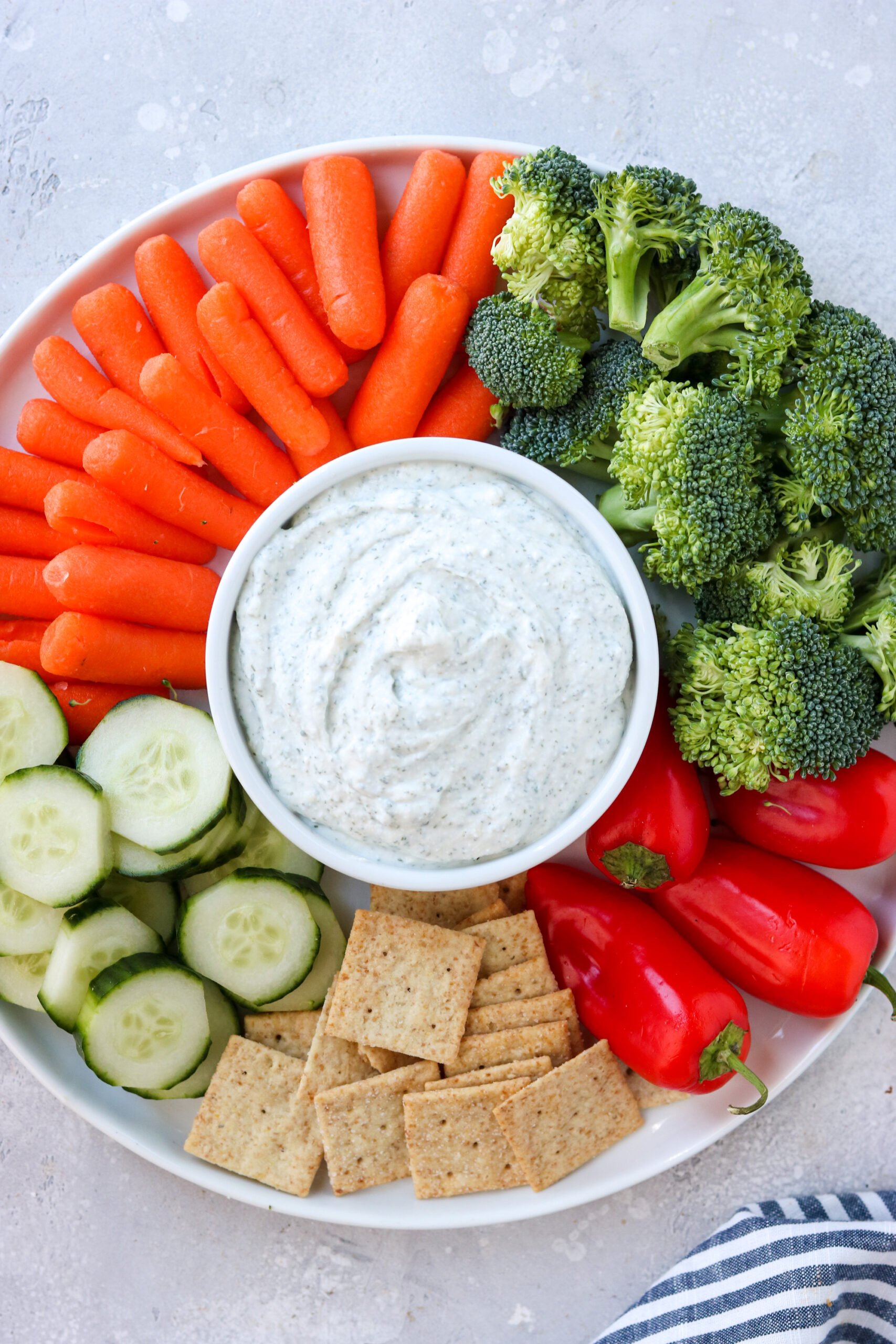 a platter of vegetables and crackers with a small bowl of cottage cheese dip in the middle. 