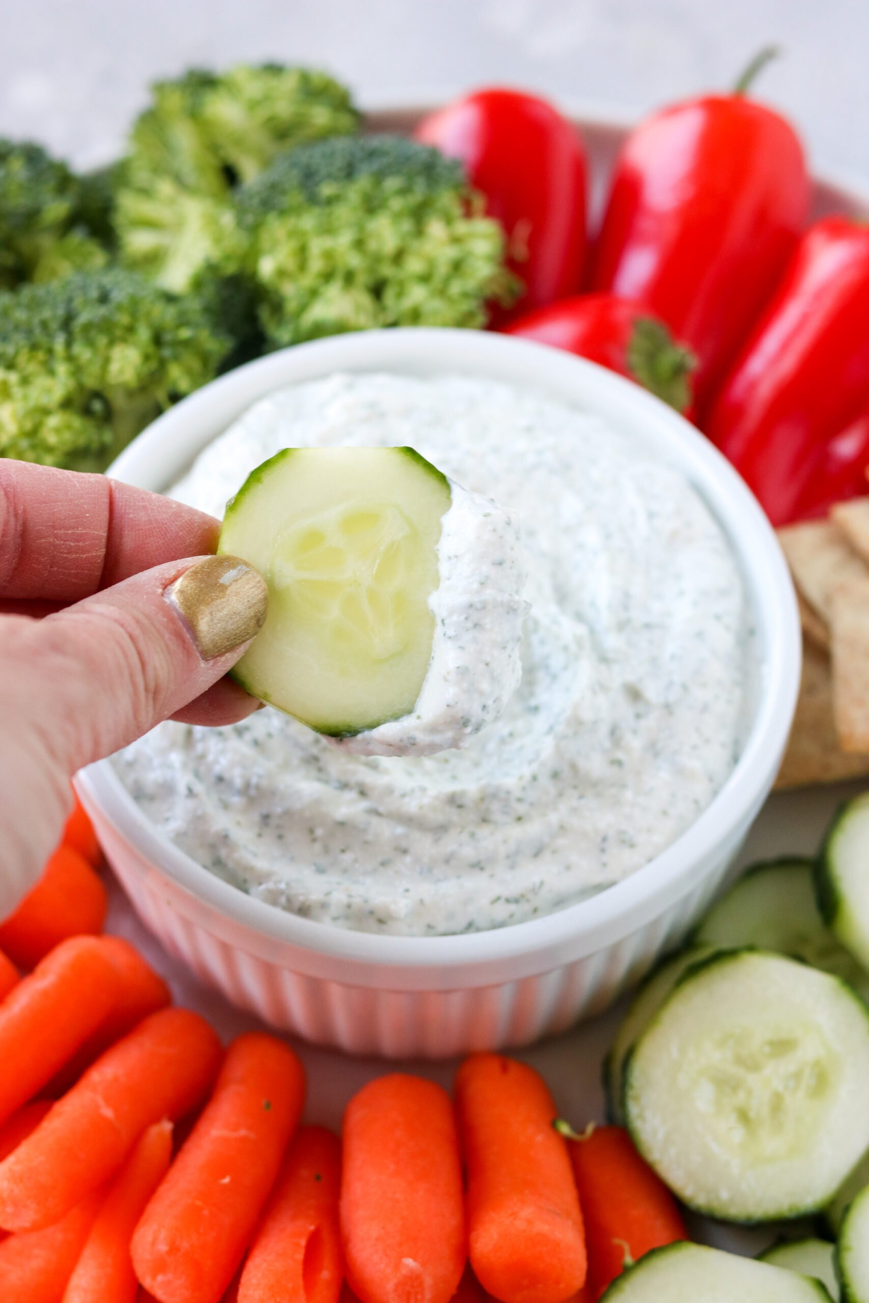 a hand holding a cucumber that has been dipped in cottage cheese ranch dip. 