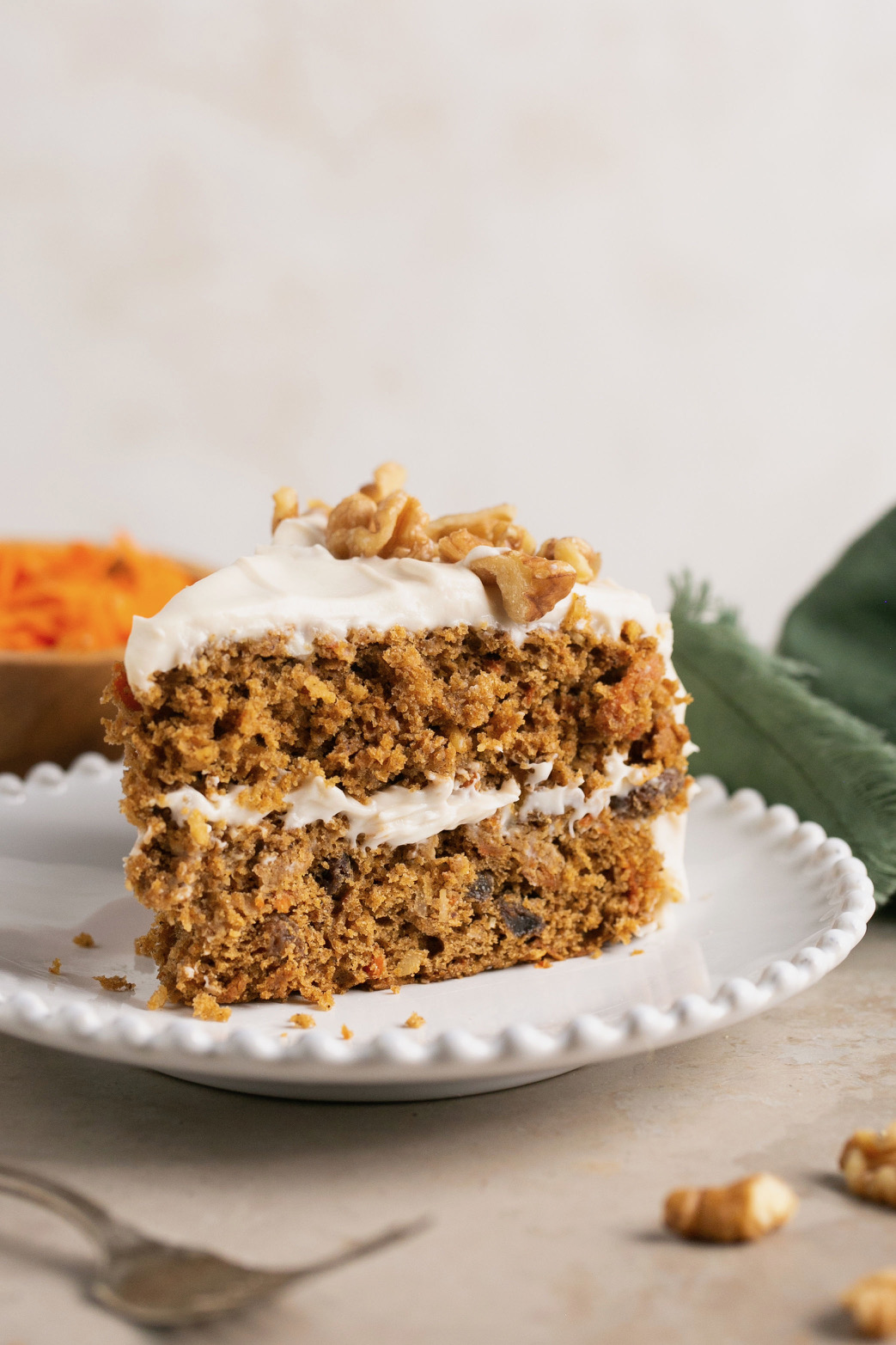 a slice of gluten free carrot cake on a white dish topped with walnuts