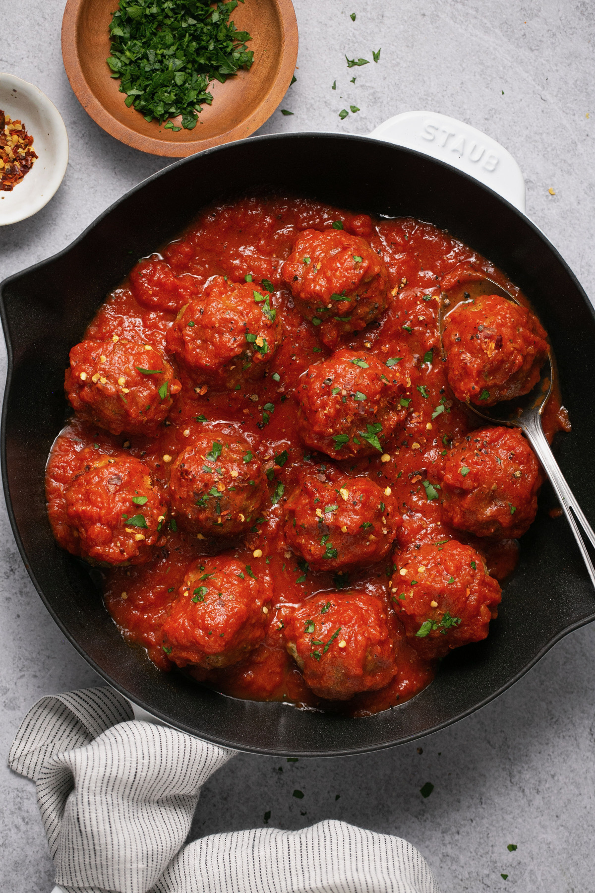 gluten free meatballs with sauce in a white and black cast iron skillet topped with parsley