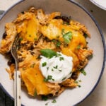 crock pot chicken enchilada casserole topped with sour cream and cilantro in a bowl with a fork