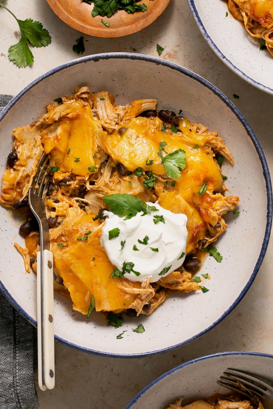 a bowl of crock-pot chicken enchilada casserole topped with chopped cilantro and sour cream