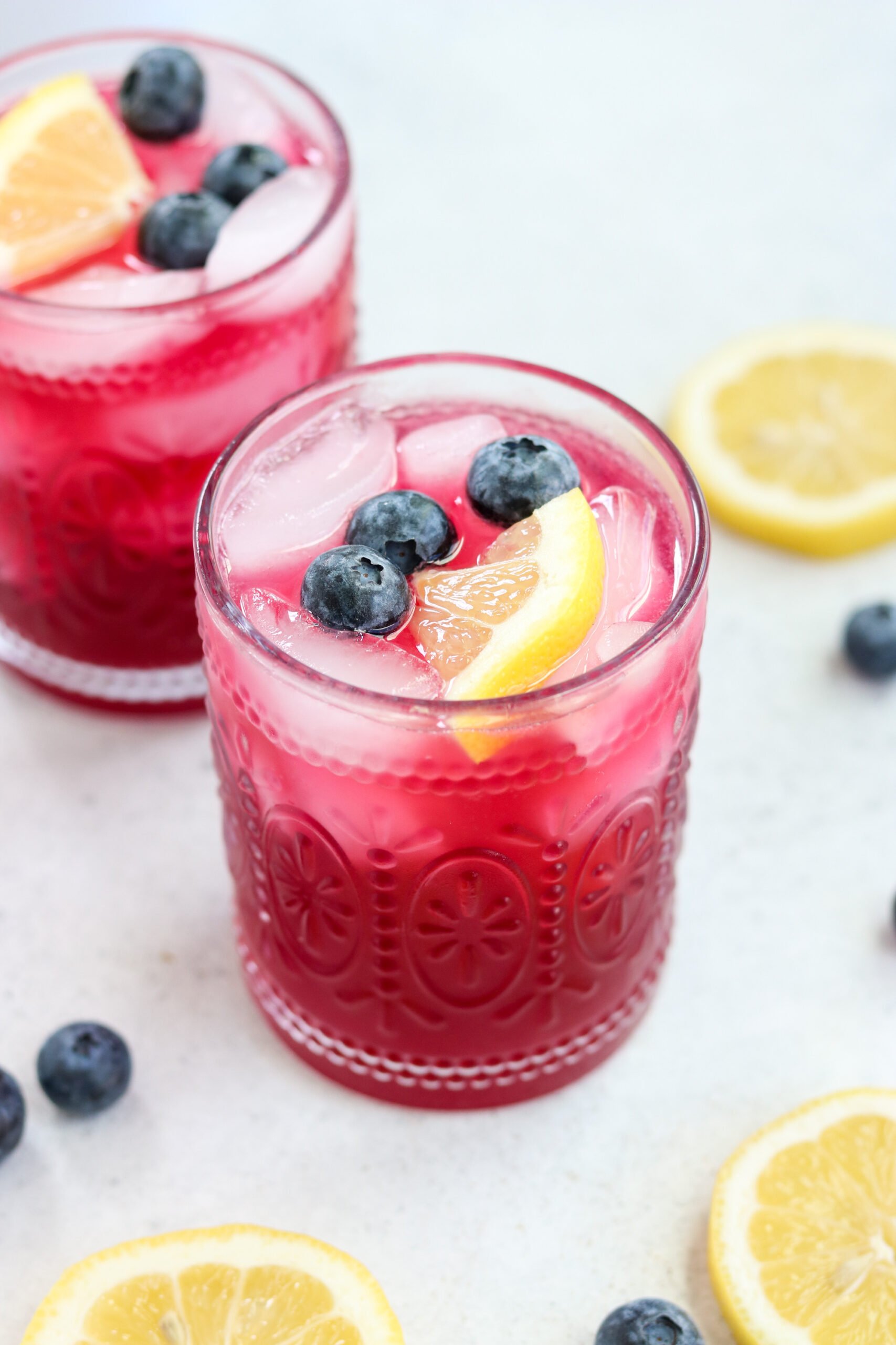 two lemon blueberry mocktails in clear glasses with ice cubes and topped with fresh blueberries and lemon slices. 