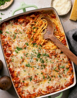 gluten free spaghetti alfredo bake in a casserole dish with a serving spoon taking a scoop out