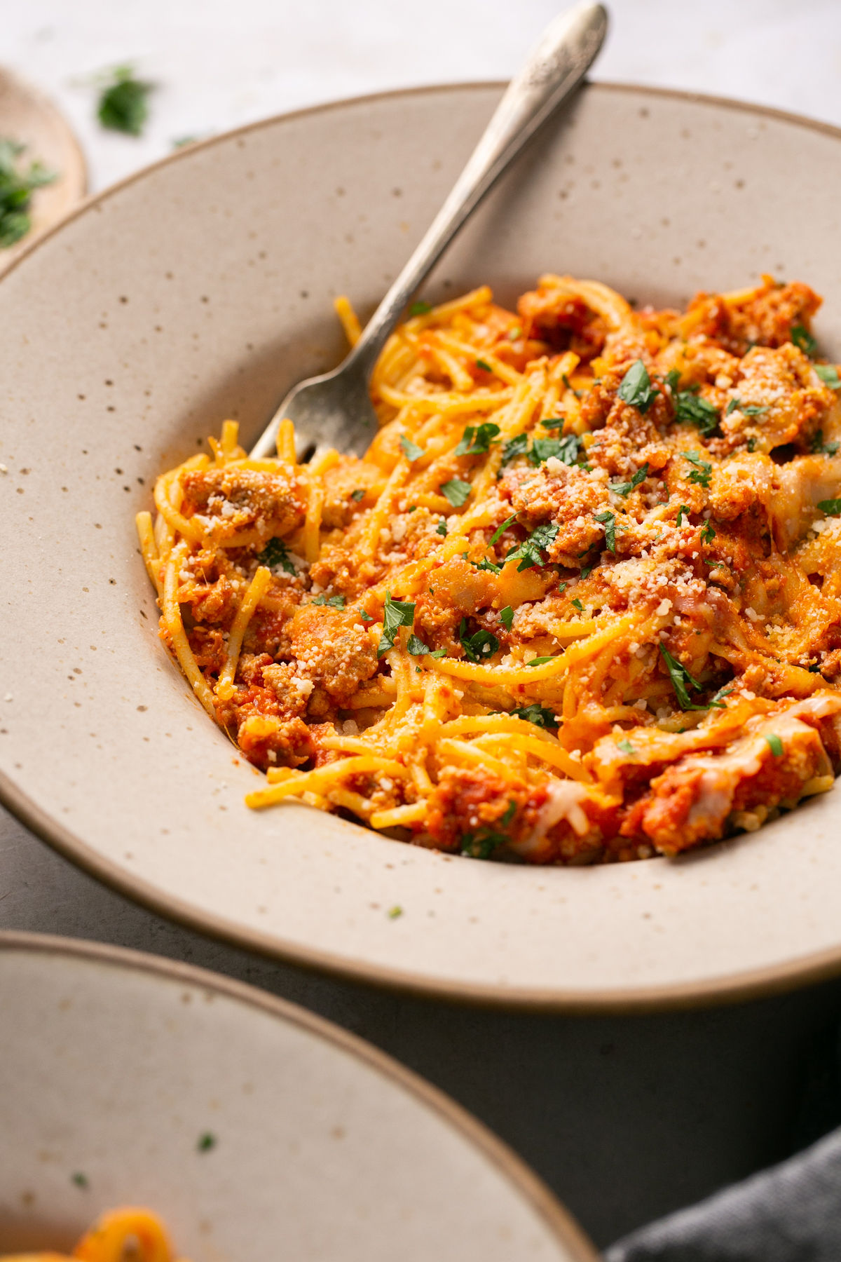 a plate with a serving of baked spaghetti topped with chopped basil and parmesan cheese.