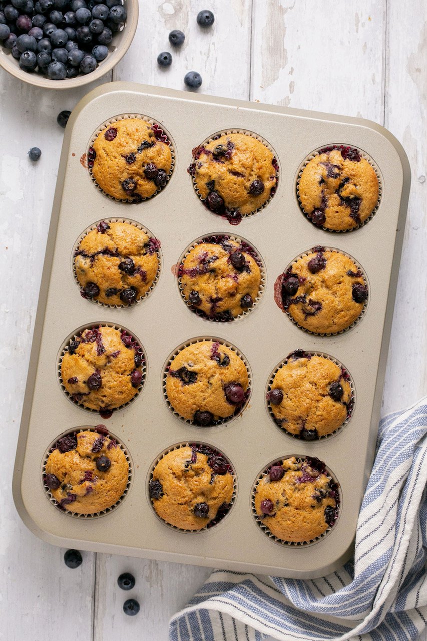 an overhead shot of a muffin tin with baked blueberry muffins. 