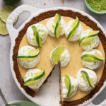 Gluten free key lime pie in a white Staub pie plate surrounded by ingredients with a slice taken out