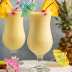 a pina colada mocktail in a fun glass with a pineapple, cherry and umbrella for garnish