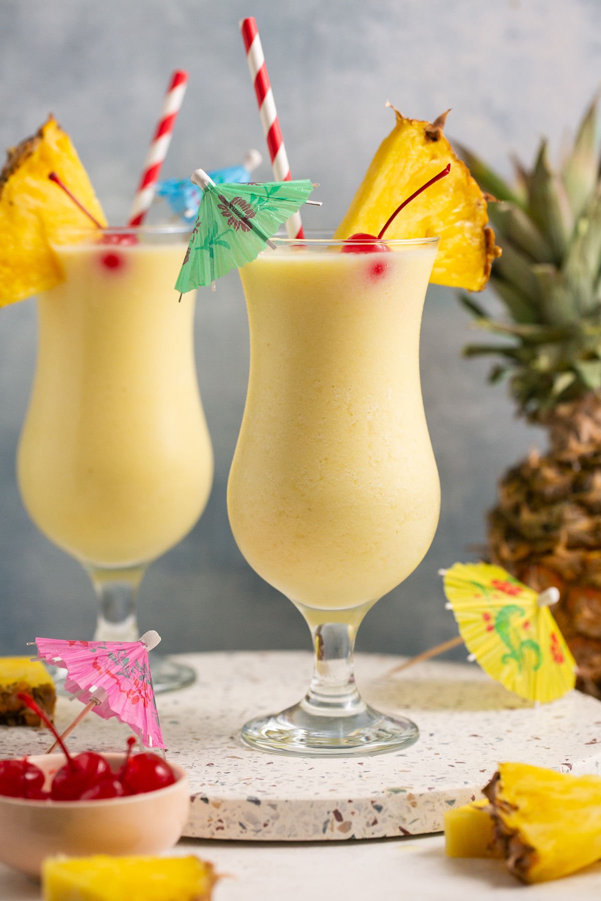 two piña colada mocktails garnished with cherries, pineapple wedges, and cocktail umbrellas. 
