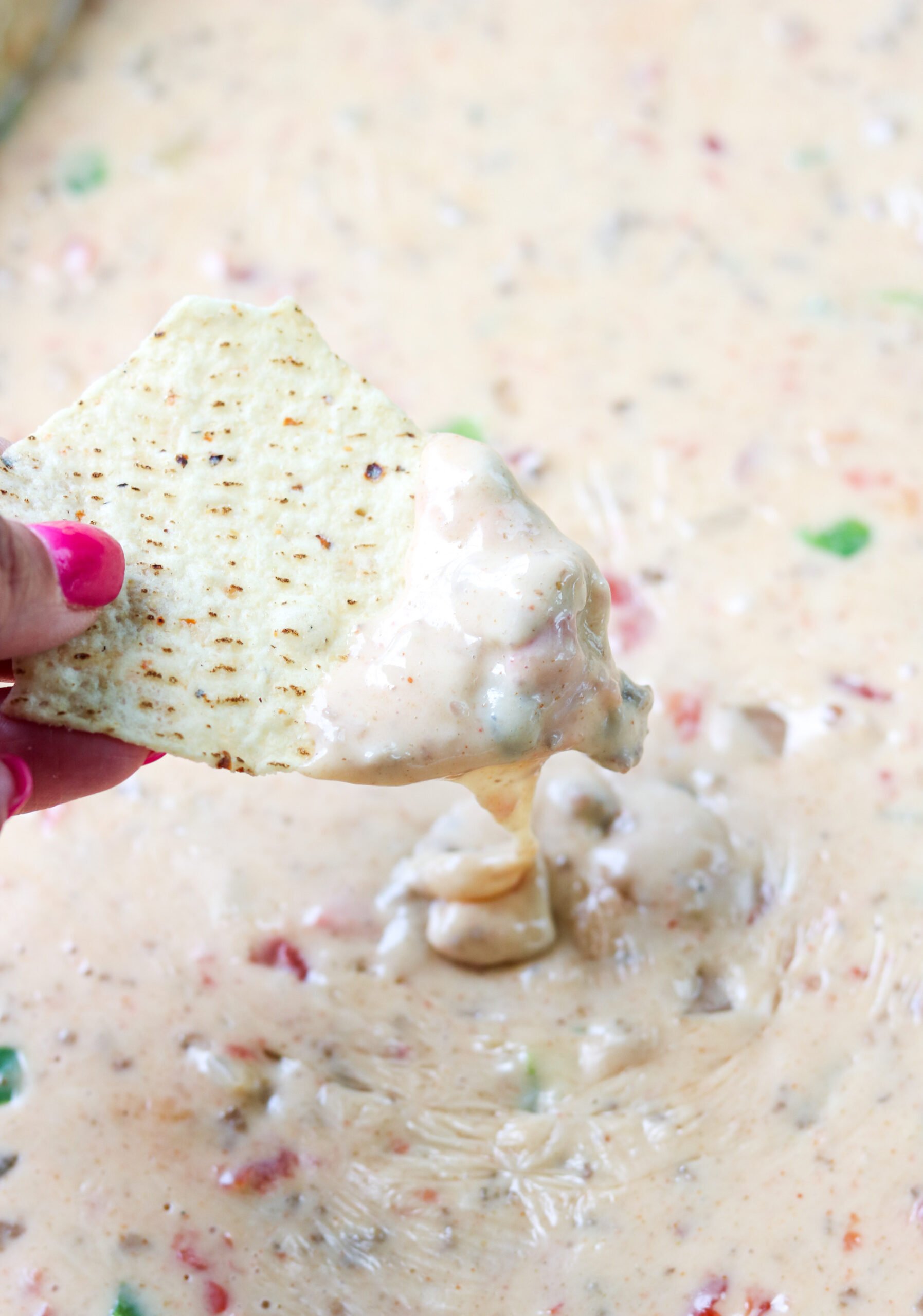 a hand dipped a tortilla chip into smoked queso dip.