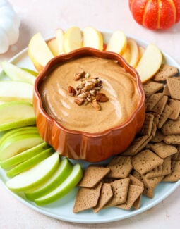 pumpkin cream cheese dip in a pumpkin-shaped bowl on a plate with apples and sweet thins