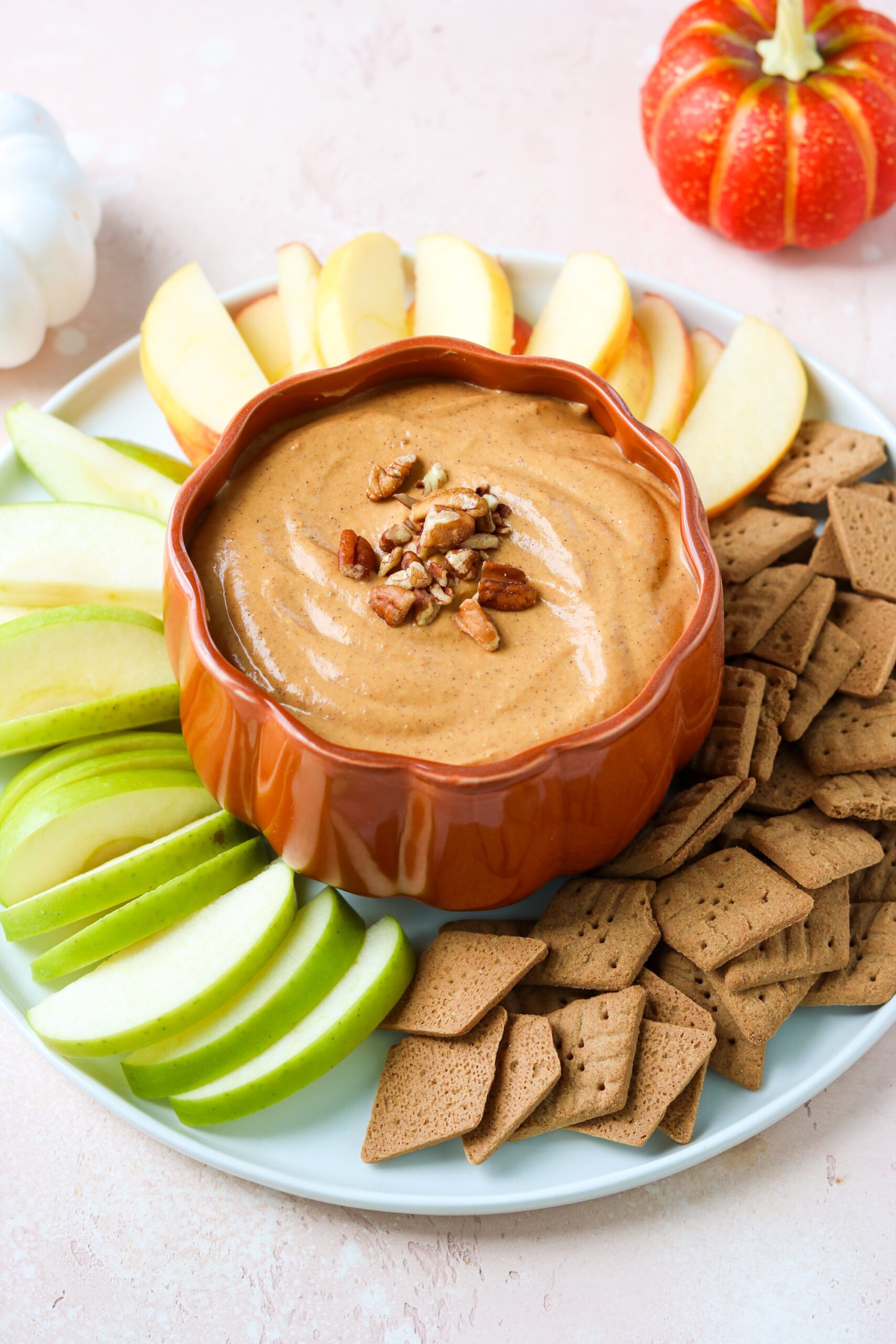 pumpkin cream cheese dip in a pumpkin-shaped bowl on a plate with apples and sweet thins