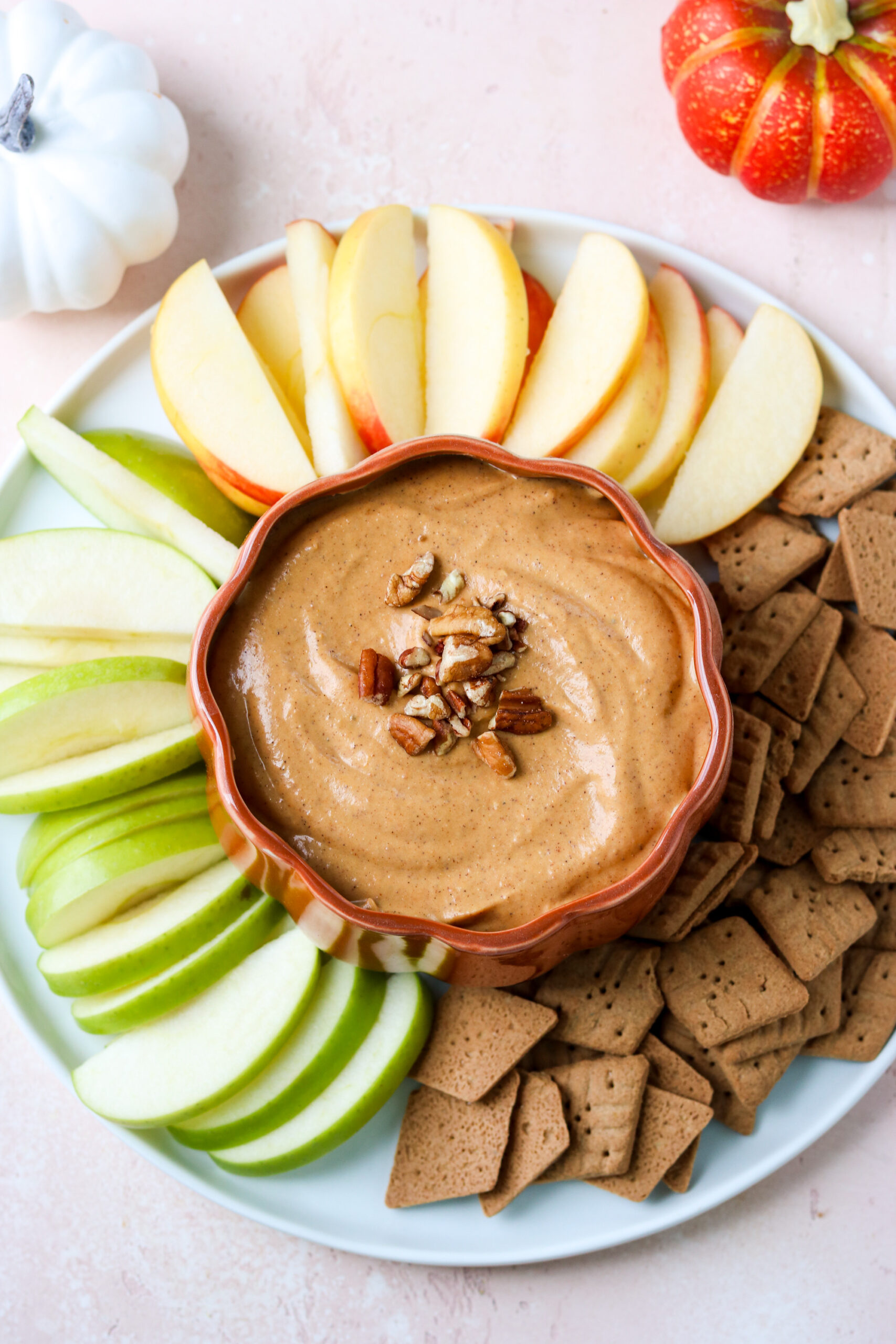 pumpkin dip in a pumpkin-shaped dish on a white plate surrounded by apples and graham crackers