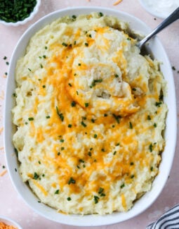 cheesy mashed potatoes in a casserole dish with a spoon taking a scoop out