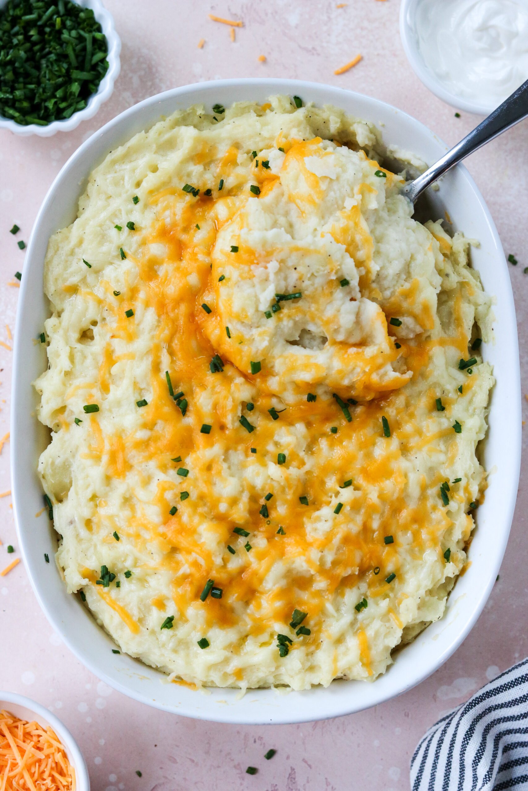cheesy mashed potatoes in a casserole dish with a spoon taking a scoop out