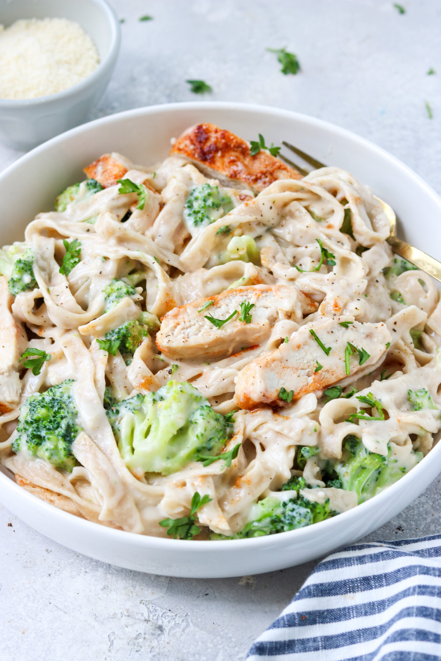 chicken and broccoli with alfredo sauce mixed with gluten free tagliatelle in a bowl topped with parsley