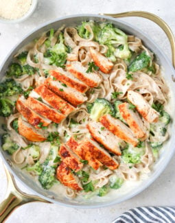 chicken and broccoli with alfredo sauce and gluten free pasta in a skillet with a napkin and a small bowl of parmesan on the side