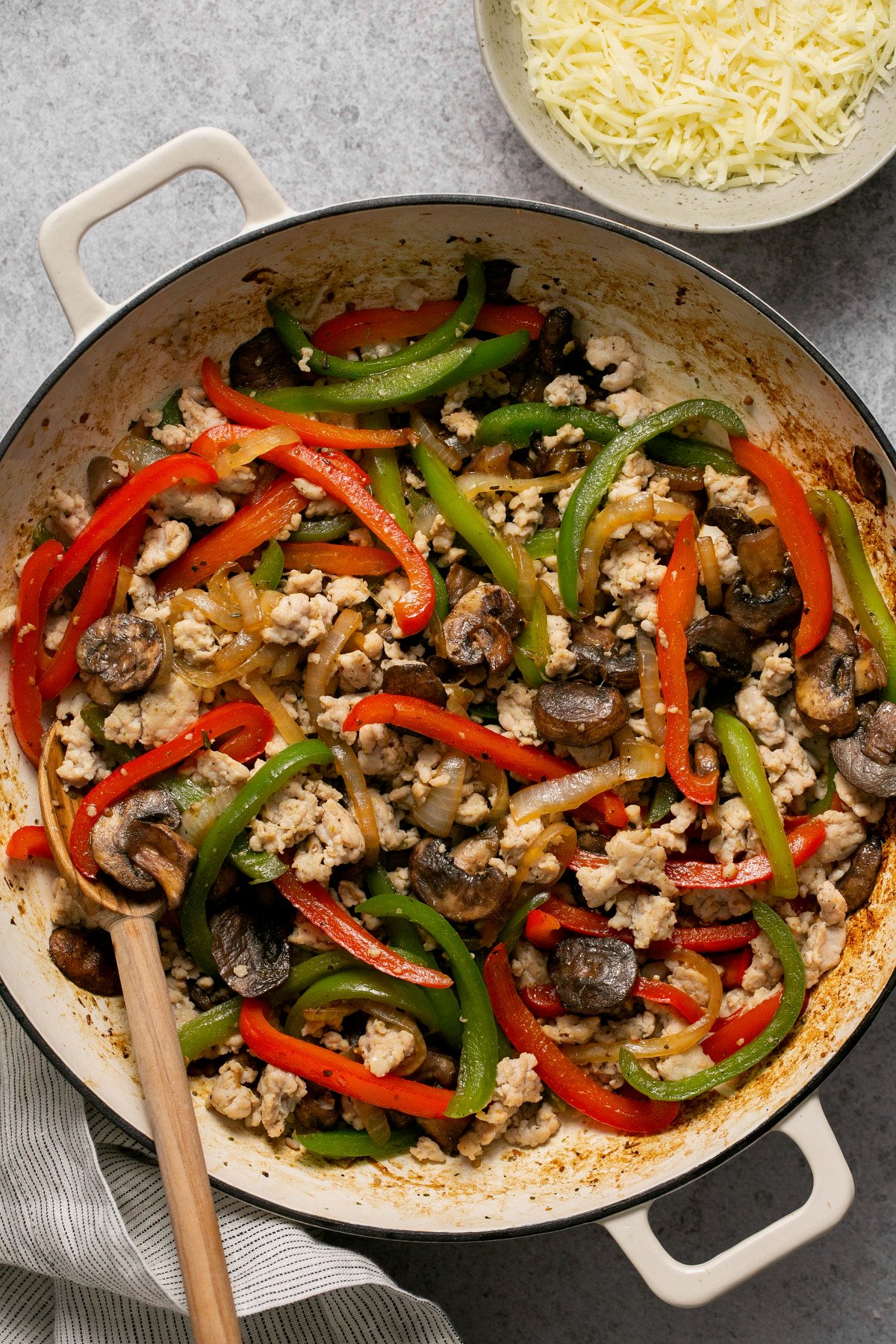 ground chicken with peppers, onions and mushrooms in a skillet with cheese on the side