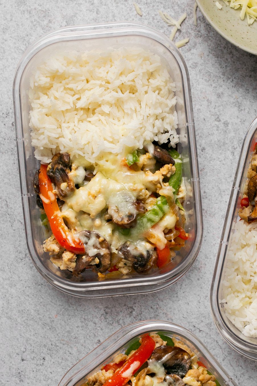 a meal prep container with chicken, veggies, rice, and cheese