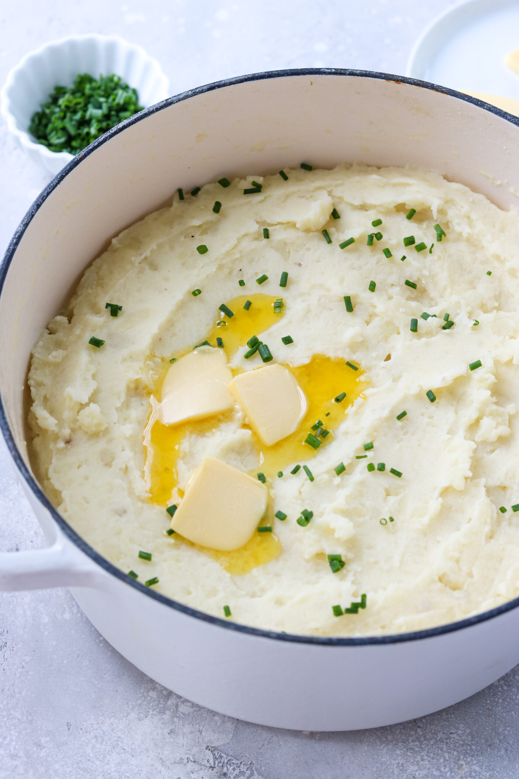 a side view of mashed potatoes in a pot topped with chives and melting butter