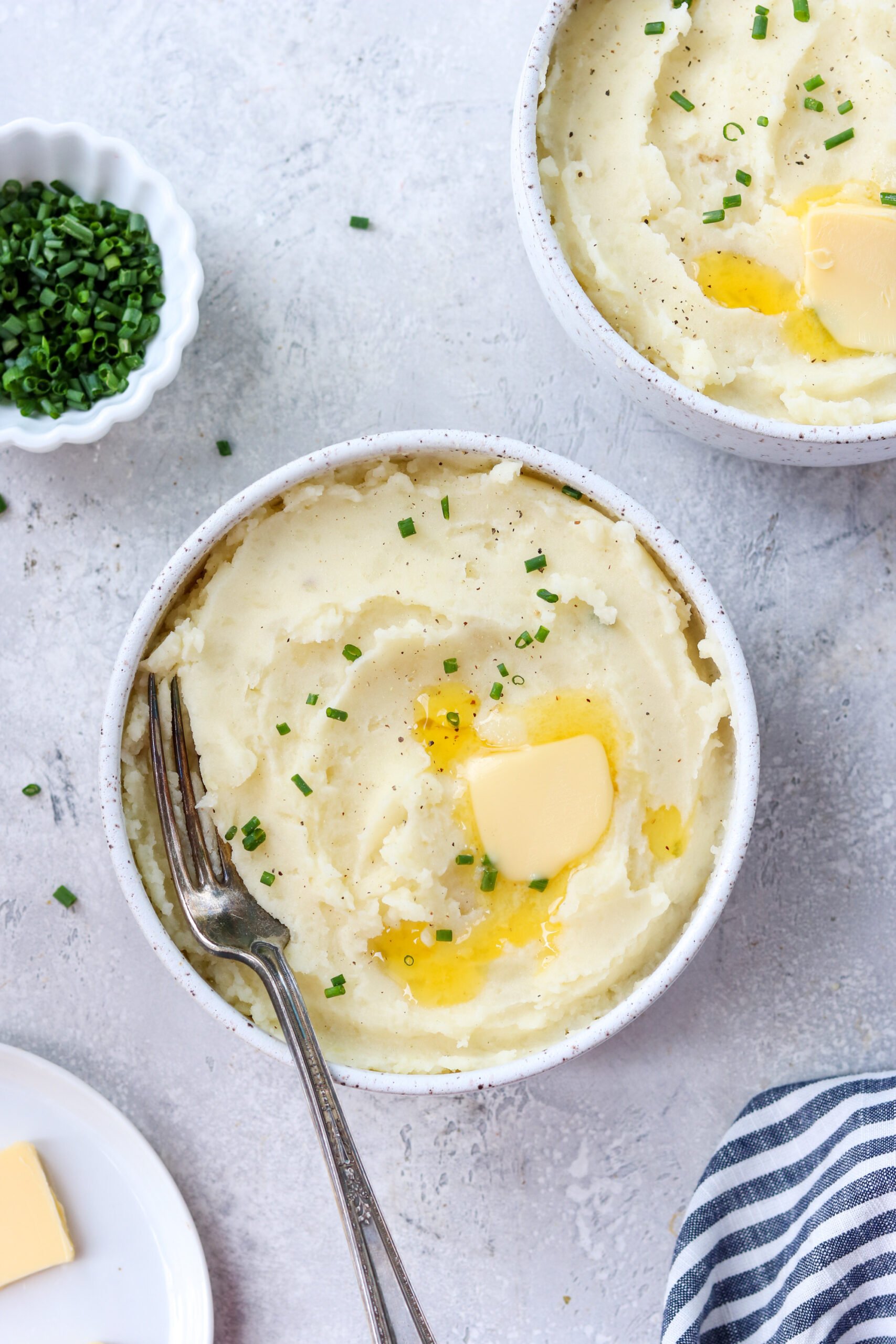 gluten free mashed potatoes in 2 bowls with chives and butter on the side