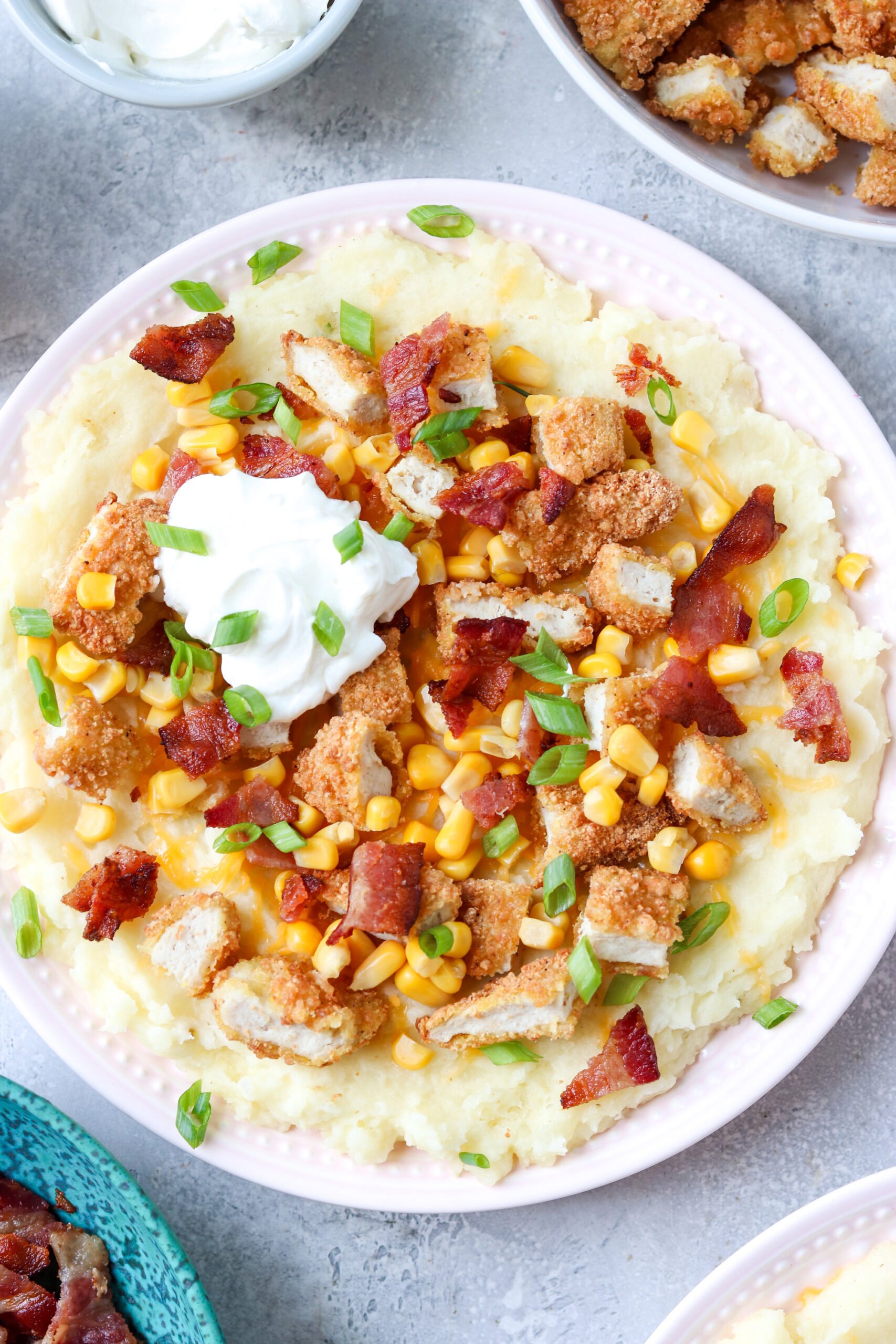 gluten free loaded potato bowl with mashed potatoes, cheese, bacon, corn, chicken tenders, bacon, and green onions with a dollop of sour cream