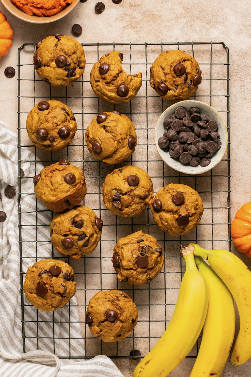 pumpkin banana muffins on a wire cooling rack next to a small bowl of chocolate chips