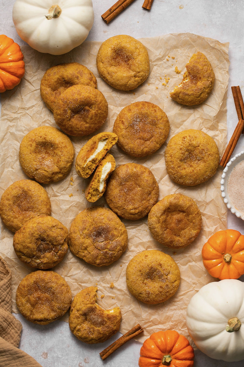 pumpkin cheesecake cookies on parchment paper with mini orange and white pumpkins