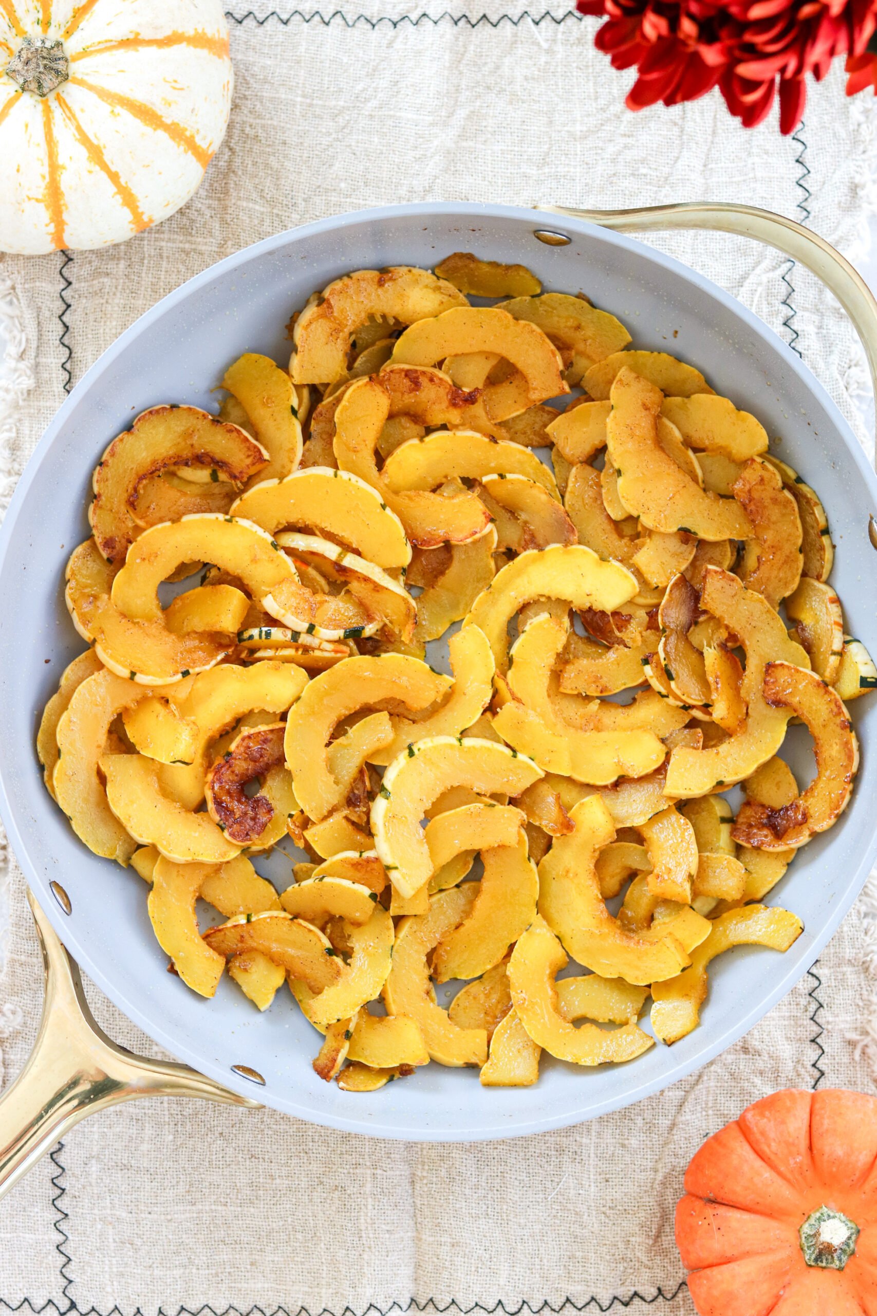 sauteed delicata squash in a skillet surrounded by pumpkins