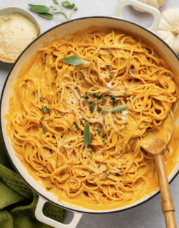 pumpkin pasta sauce with spaghetti in a pan with a wooden spoon topped with sage