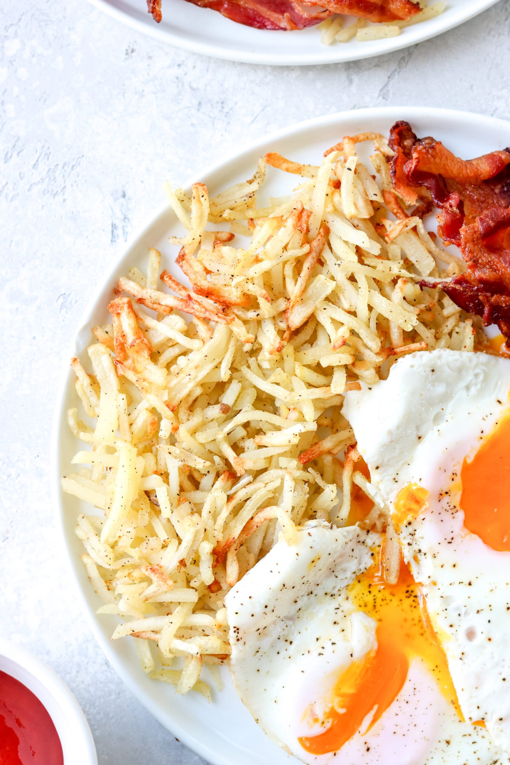 a close up of cooked hash browns on a plate with eggs and bacon