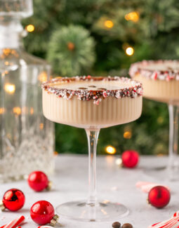 peppermint espresso martini with a candy cane rim with a Christmas tree in the background surrounded by ornaments