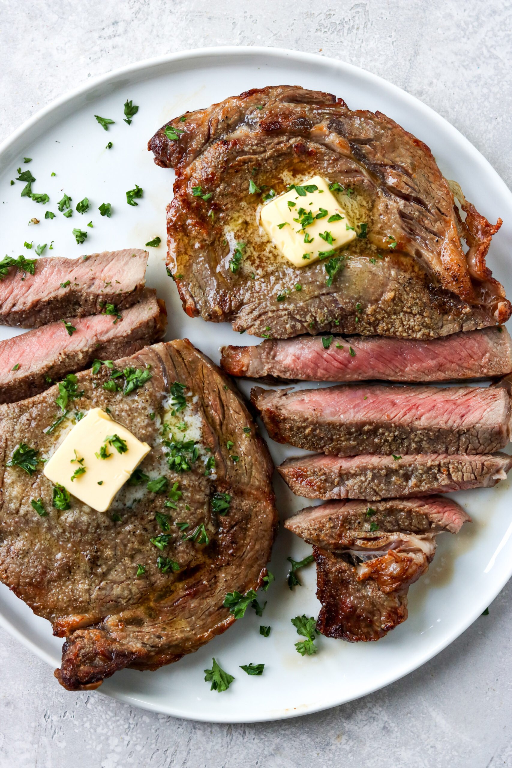 sliced ribeye steak on a white plate topped with butter and parsley