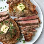 sliced air fryer ribeye steak on a white plate topped with butter and parsley