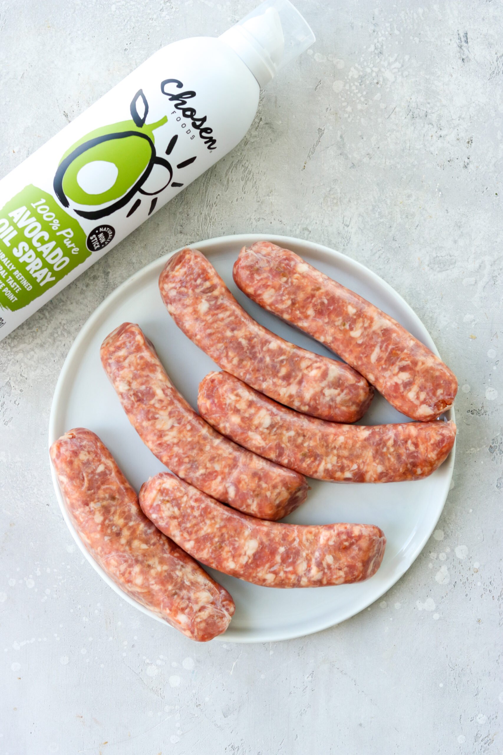raw sausages on a plate with avocado oil next to it