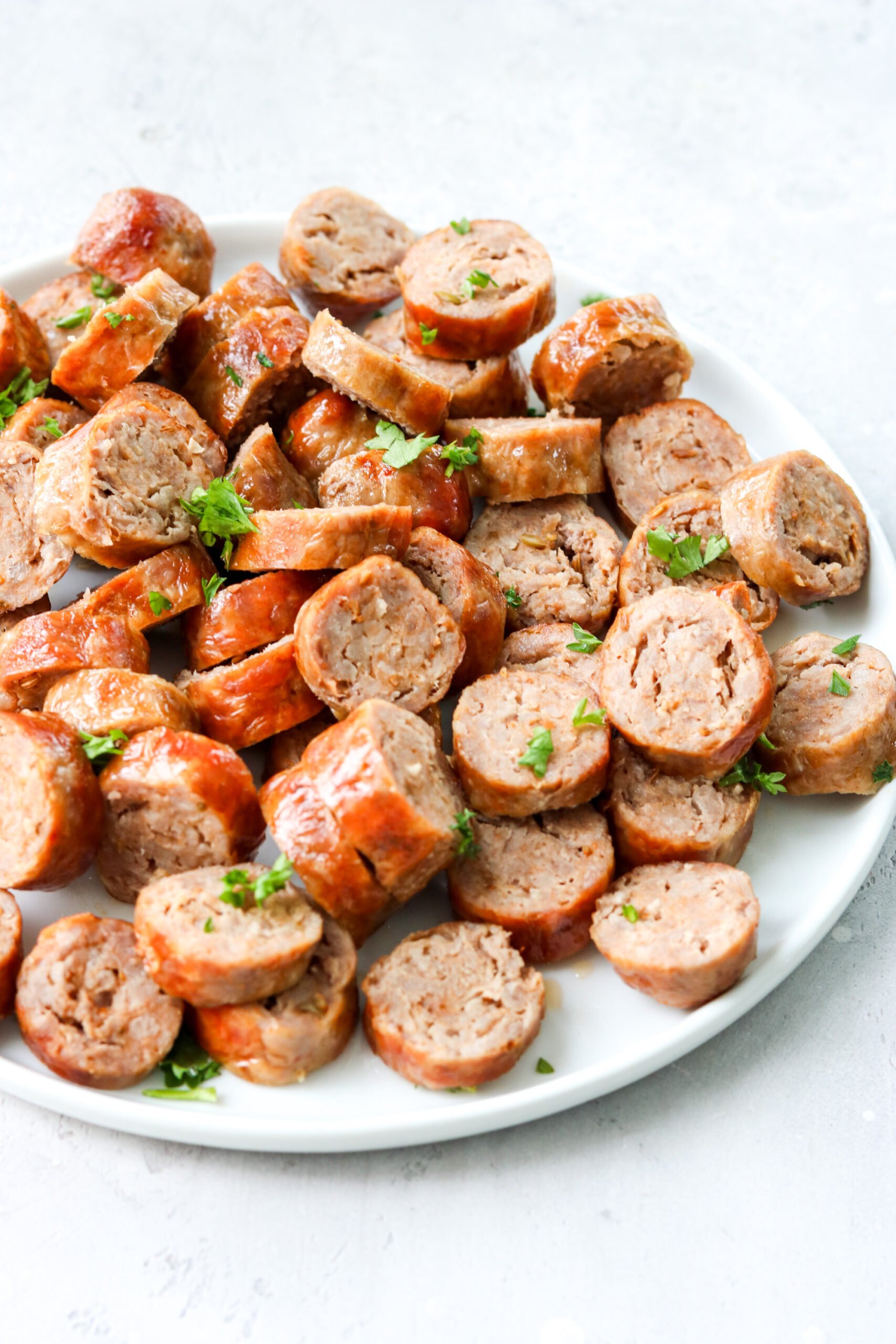 cut up Italian sausages on a white plate topped with parsley