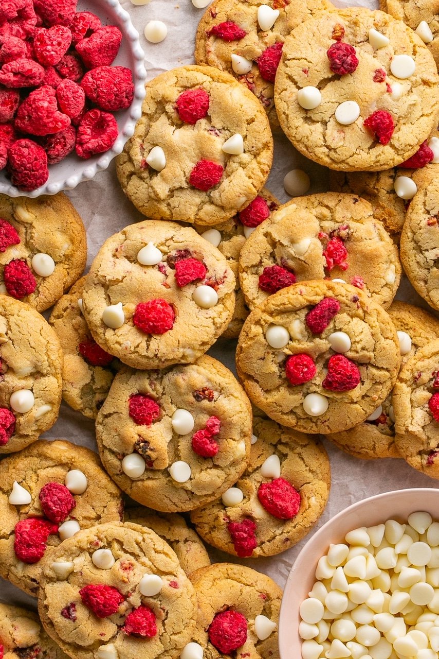 raspberry and white chocolate chip cookies spread out with a bowl of dried raspberries and white chocolate next to them