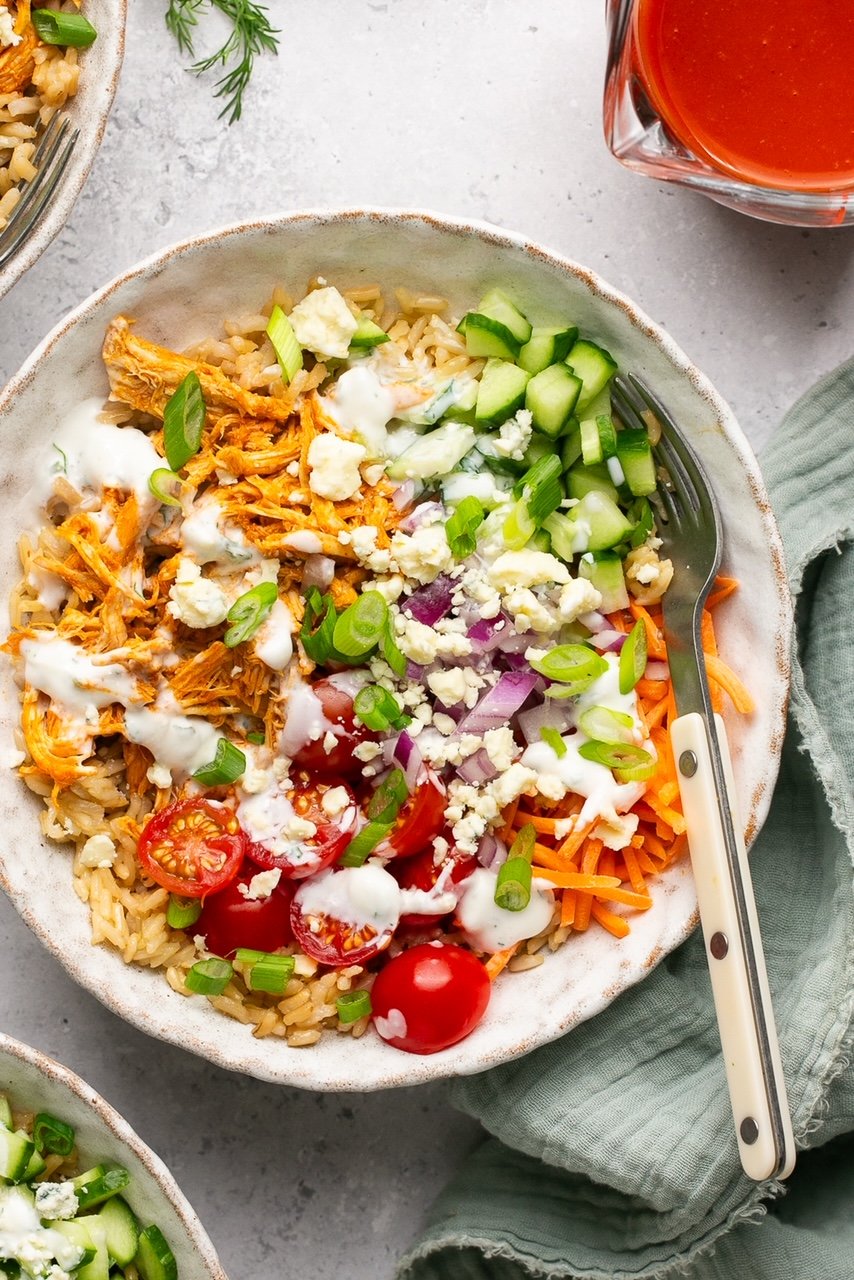buffalo chicken and rice bowls with veggies and ranch in a bowl on a gray napkin