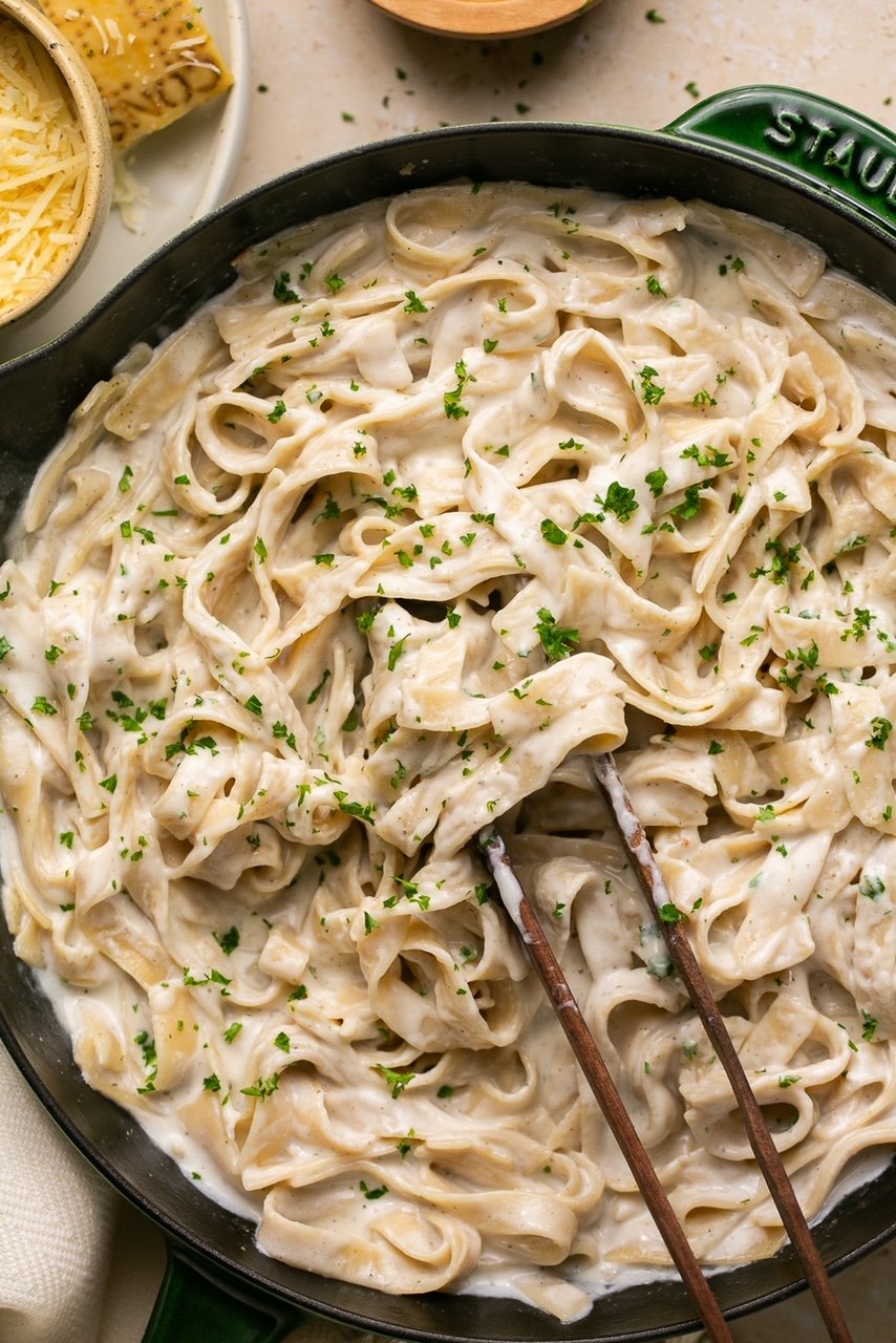 pasta with alfredo sauce in a cast iron skillet with tongs