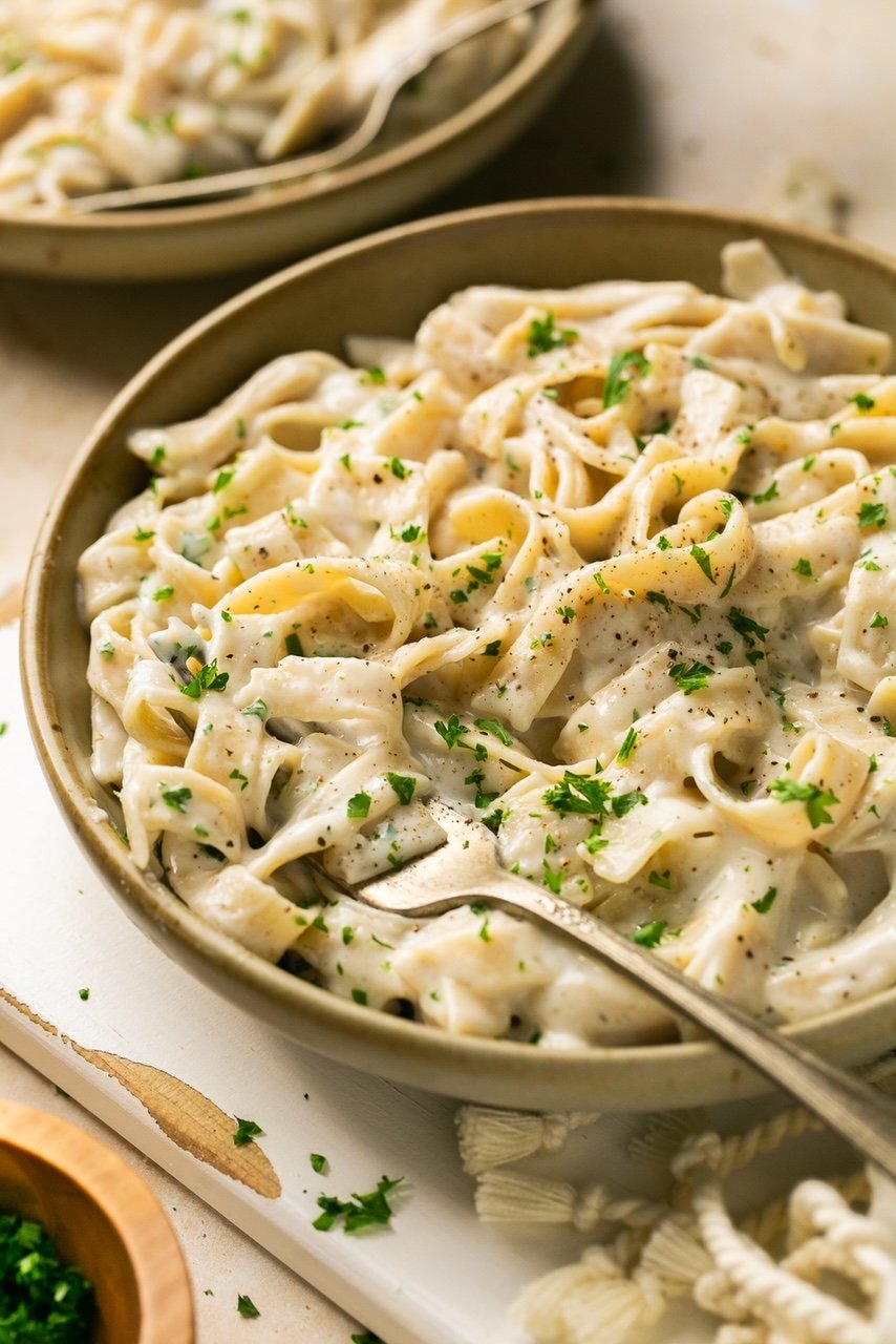 a bowl of pasta with alfredo sauce topped with parsley with a fork in it