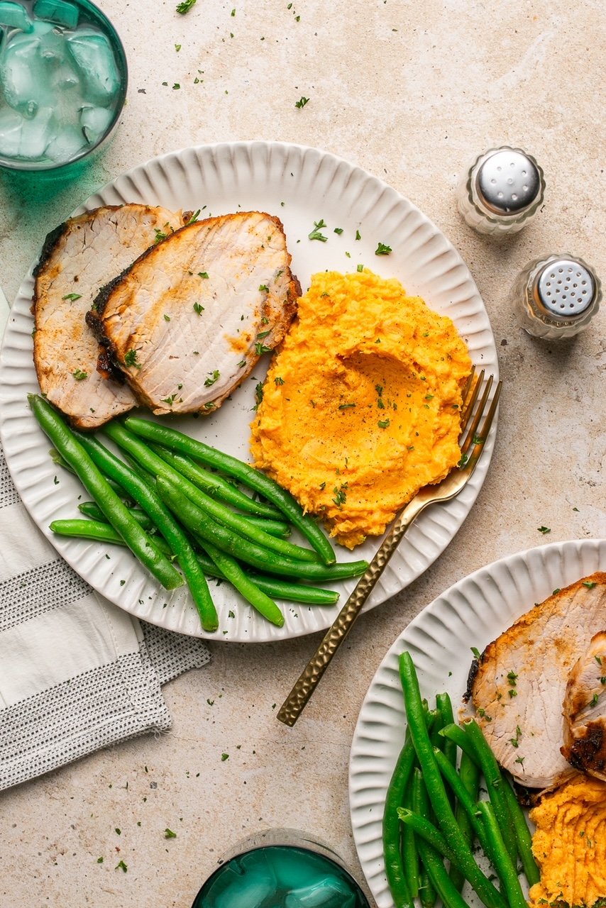 2 plates with sliced pork roast, mashed sweet potatoes and green beans