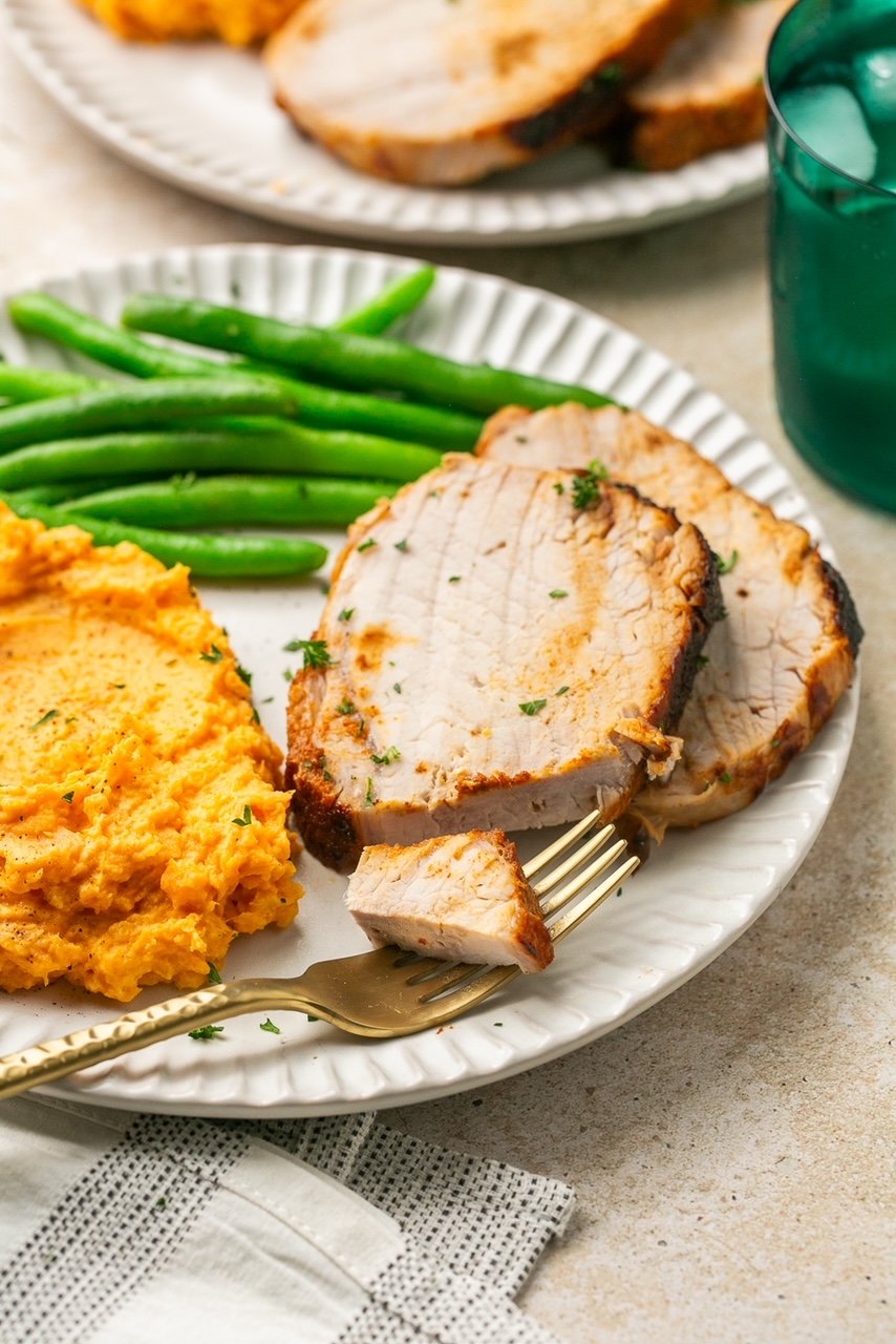 2 slices of pork roast on a plate with mashed sweet potatoes and green beans