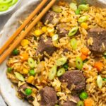 a closeup of steak fried rice in a bowl topped with green onions with chopsticks on the side