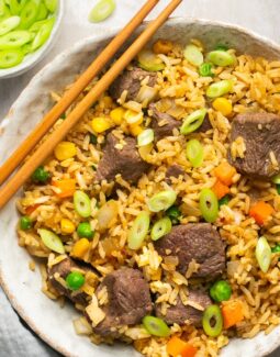 a closeup of steak fried rice in a bowl topped with green onions with chopsticks on the side