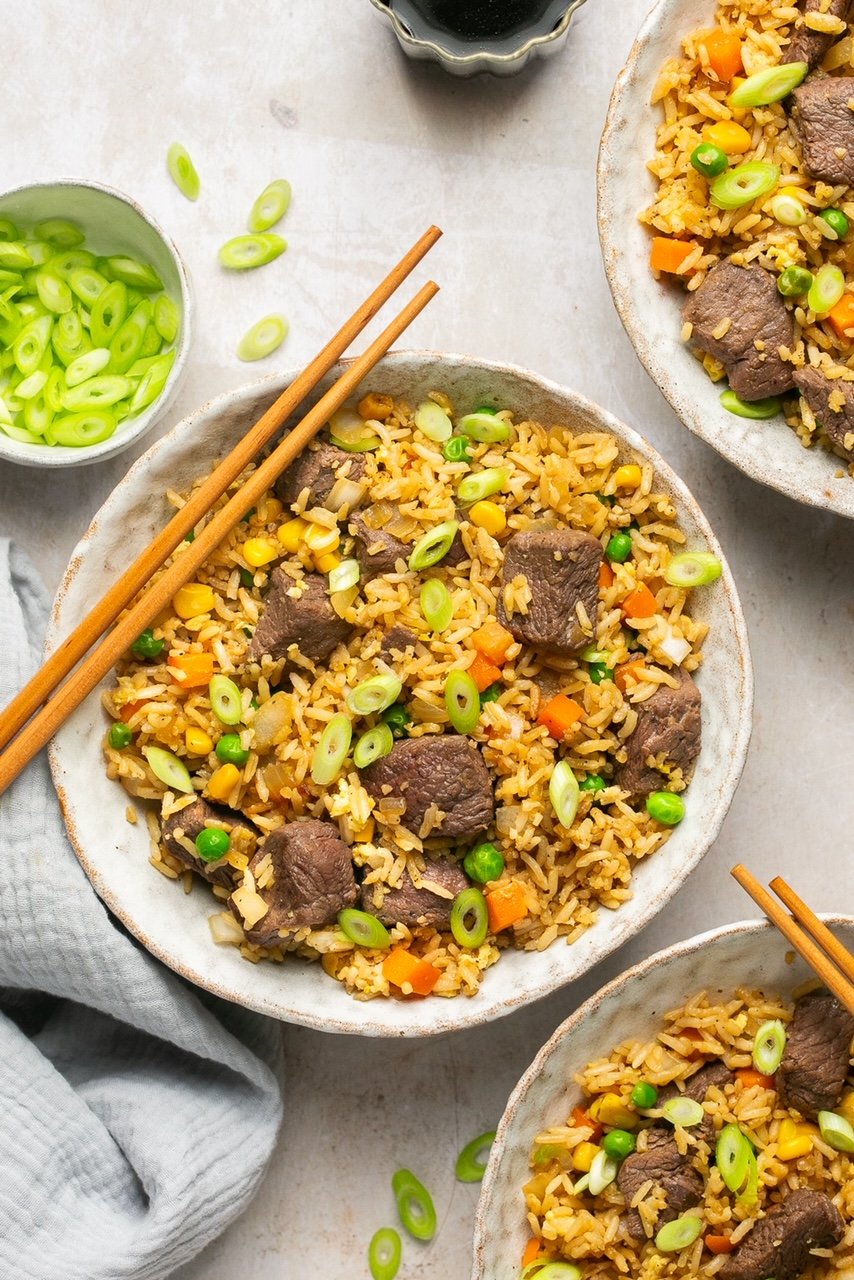 steak fried rice in bowls with chopsticks and green onions on the side